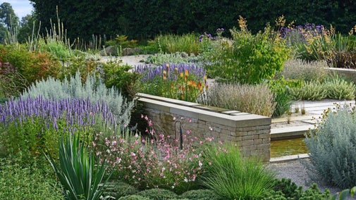 View across a gravel garden with a low stone wall and lots of colour and texture from plants and grass
